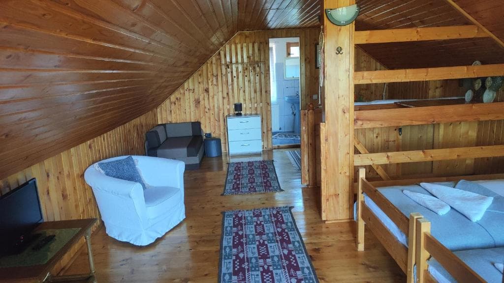 Camera Deluxe de la mansardă — fotoliu alb, paturi sub tavanul înclinat de lemn