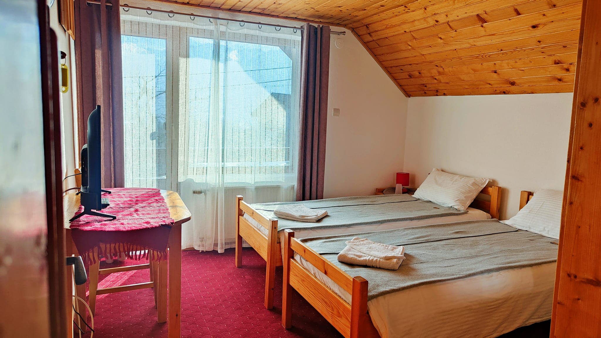 Cameră cu paturi și ușă-fereastră spre balcon, cu lumină naturală