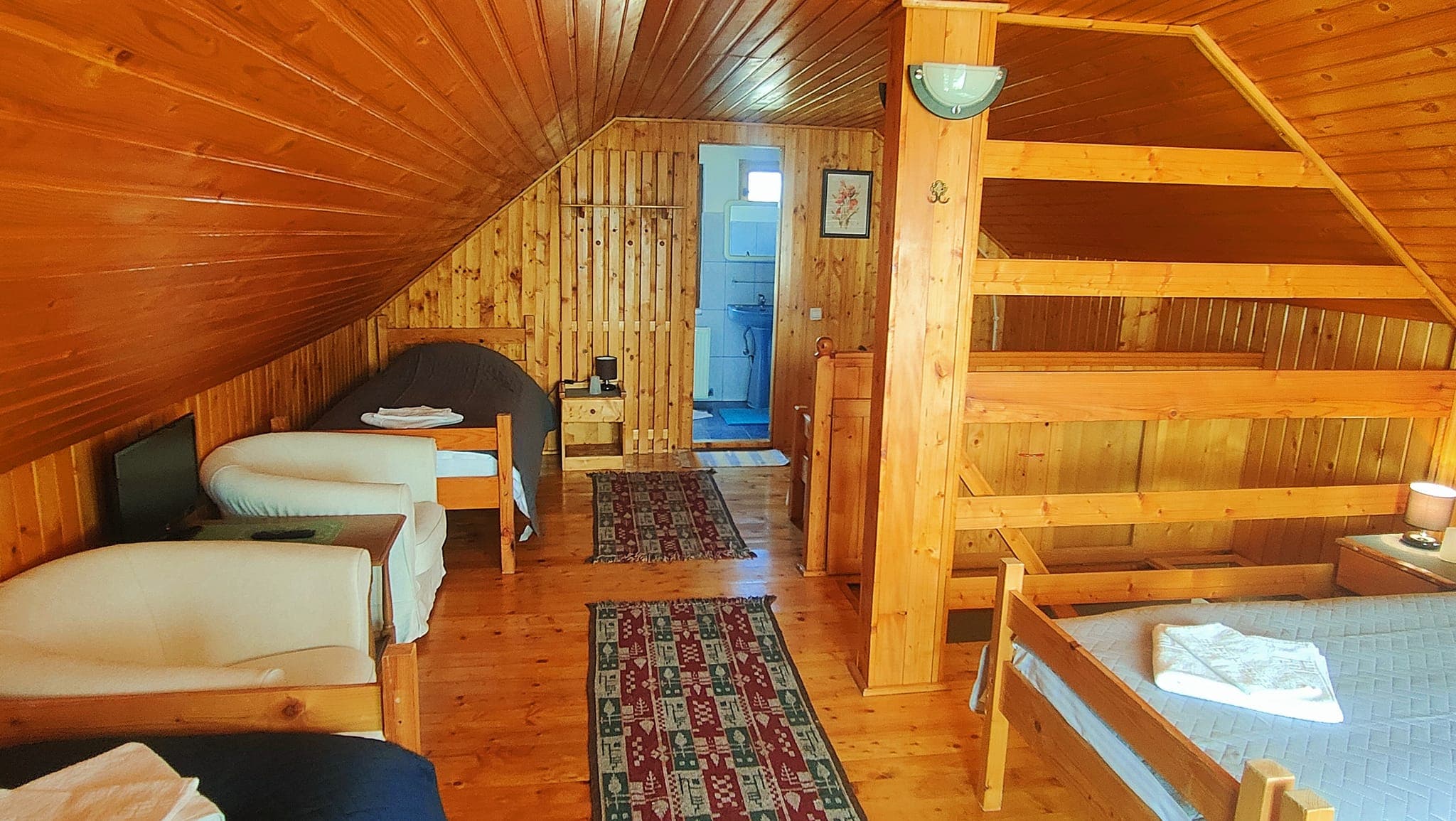 Camera de la mansardă, spațioasă, cu mai multe paturi sub tavanul de lemn
